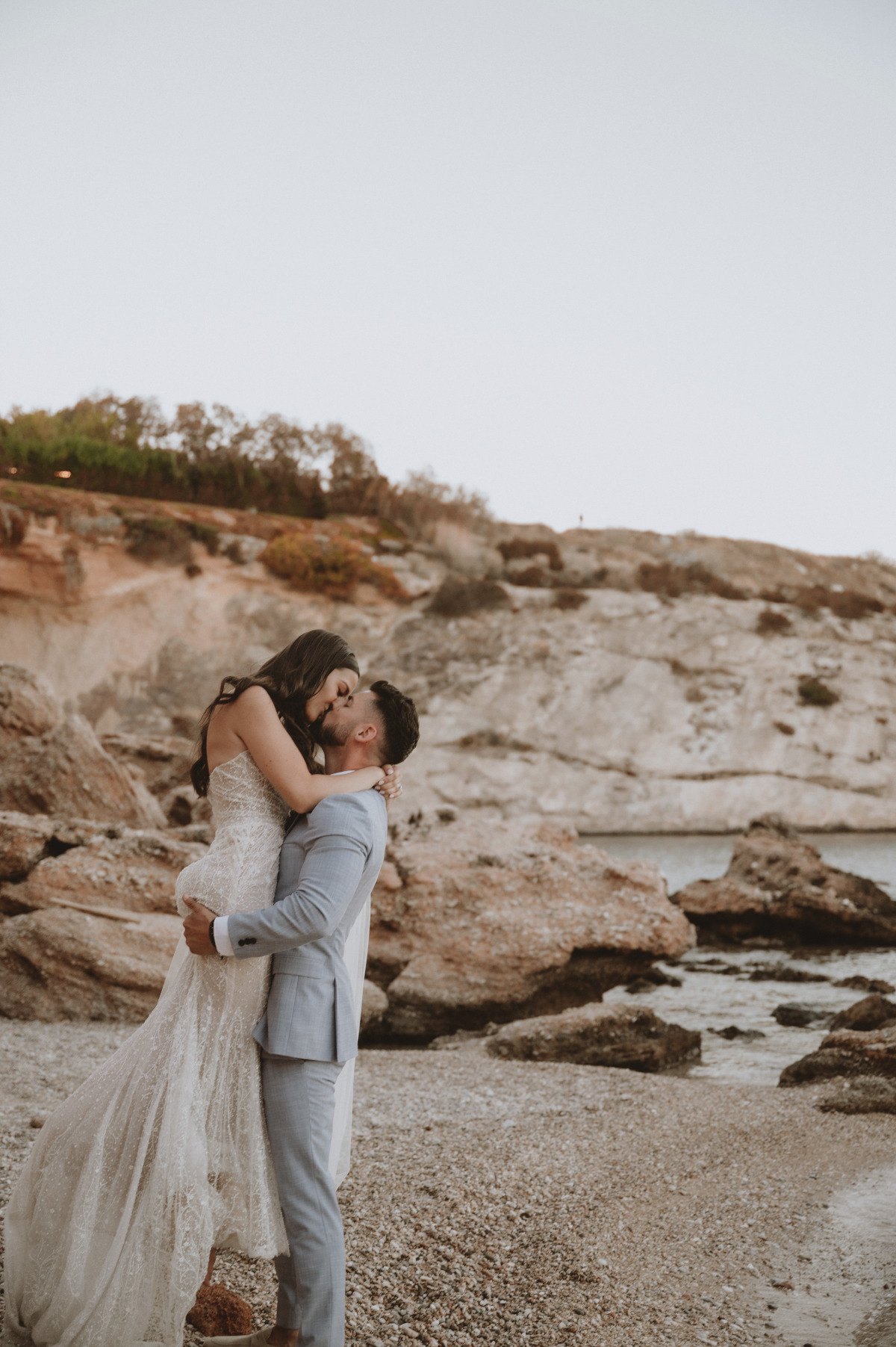 Groom holding up bride and kissing on beach at first look