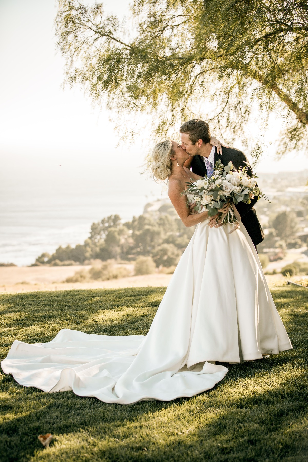 Portrait of bride and groom kissing in front of coastal view