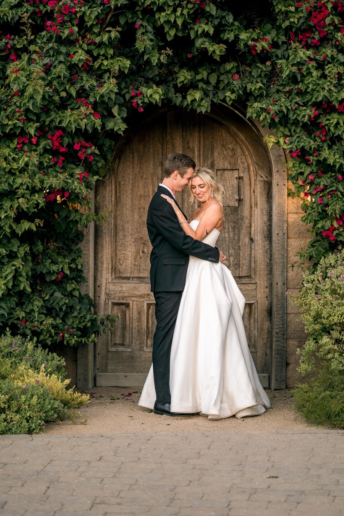 Portrait of bride and groom in front of wood door surrounded by greenery
