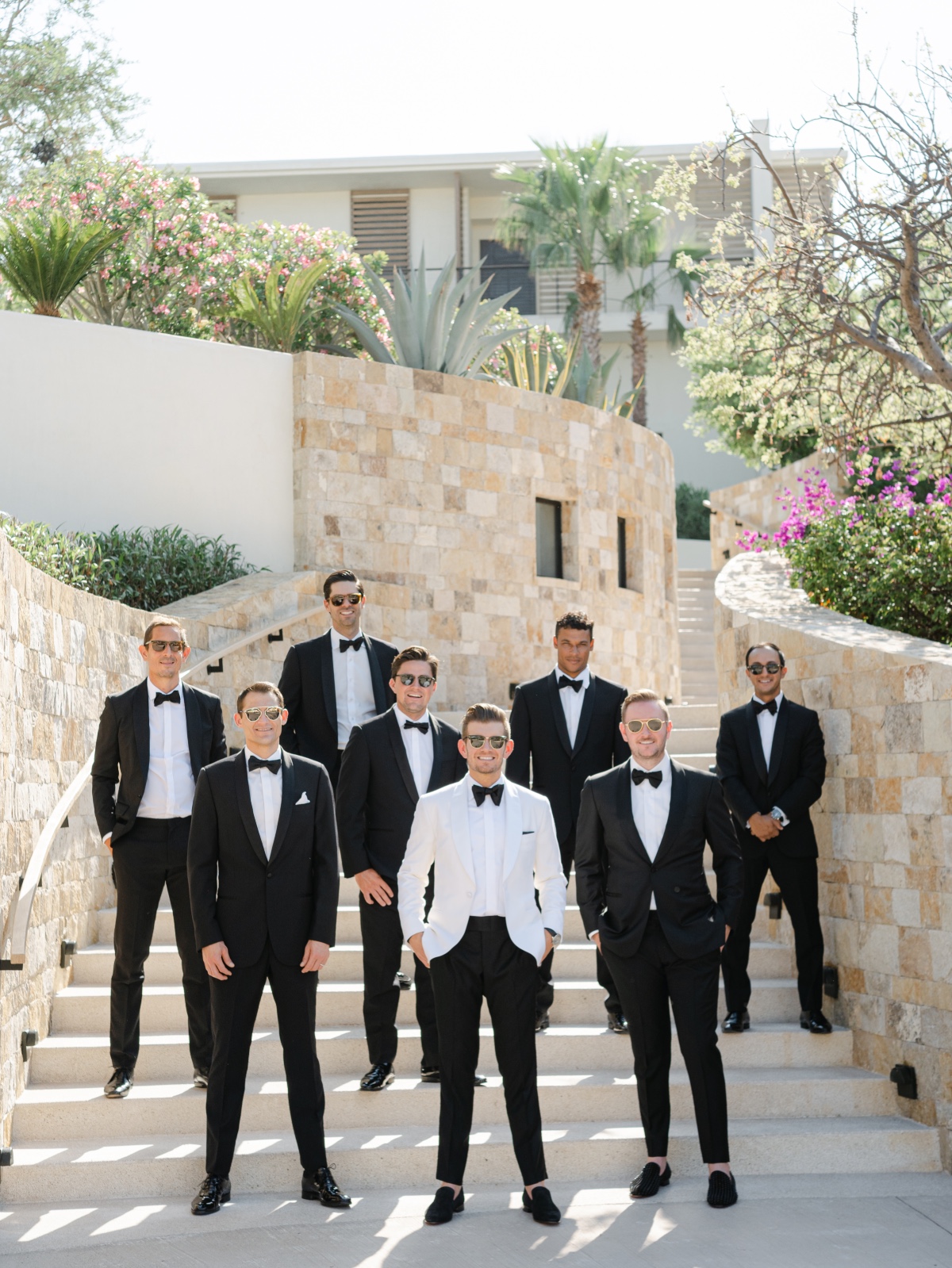 Groom in white suit jacket on steps with groomsmen in black suit jackets