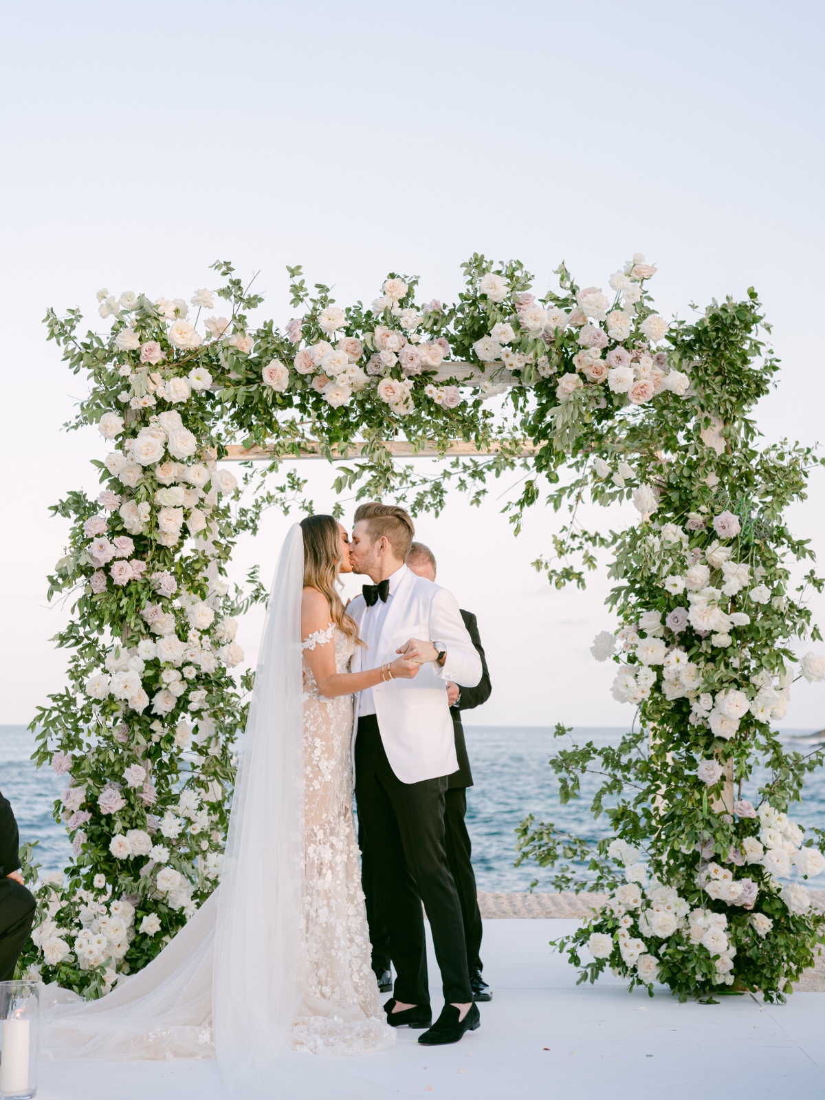 Bride and groom kissing in front of floral arch at ceremony