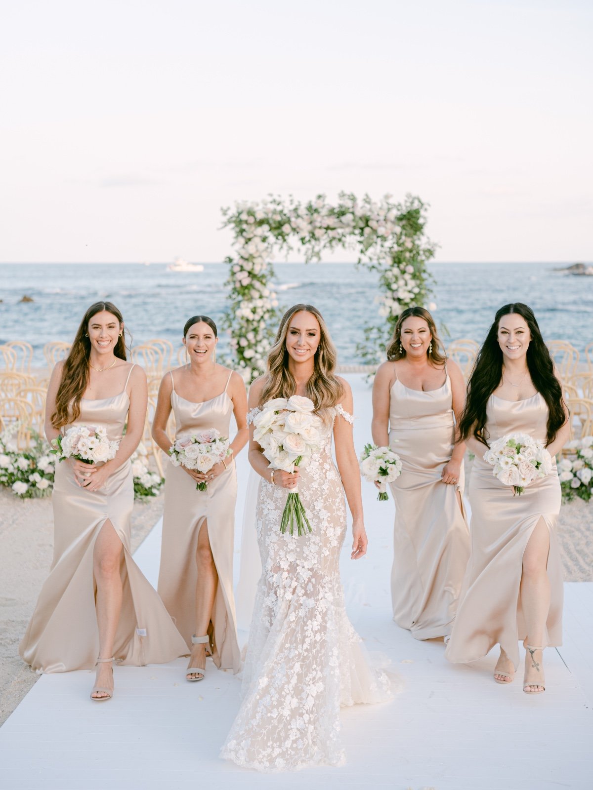 Bride and bridesmaids in champagne dresses in front of ceremony arch