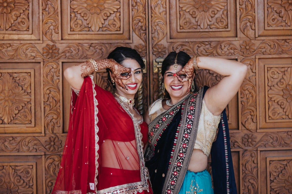 Bride and bridesmaid in traditional dresses holding fingers up to eyes
