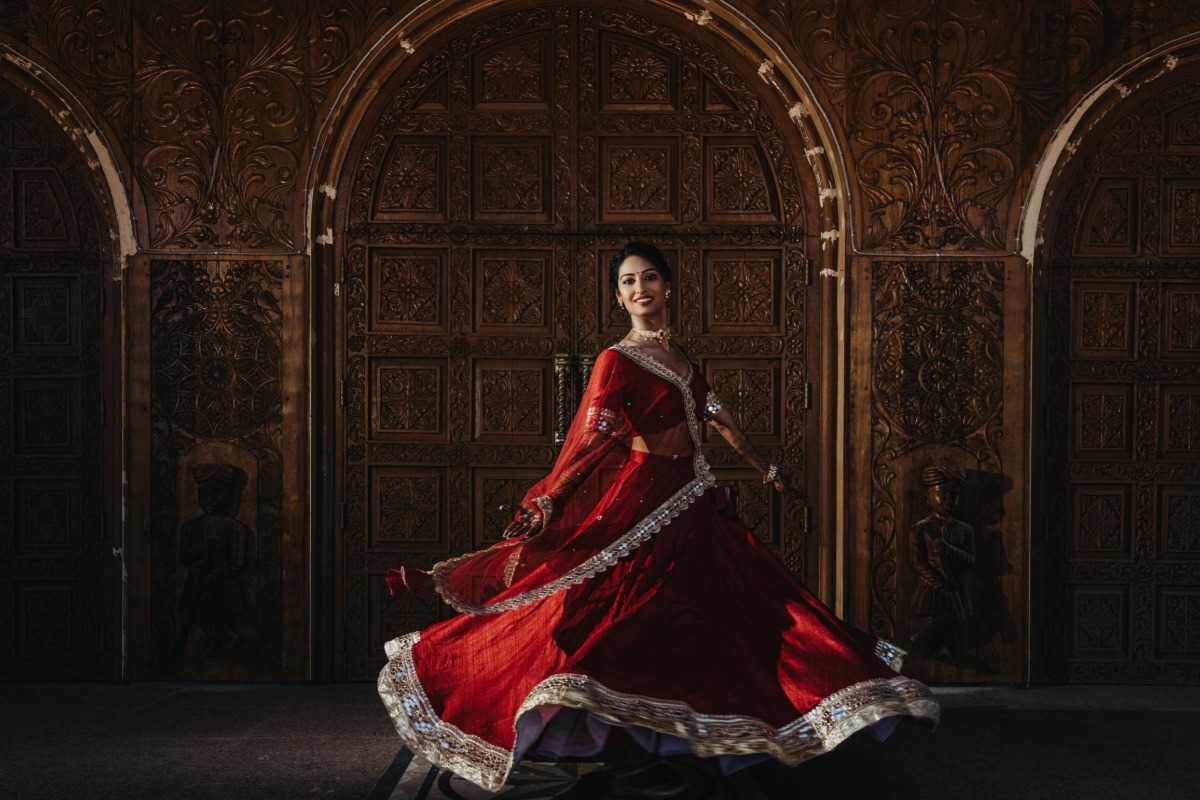 Bride spinning in front of ornate wall wearing traditional red dress