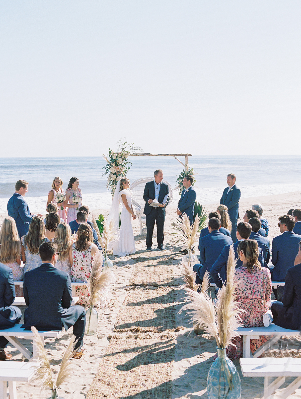 Bride and groom during ceremony on beach while guests watch