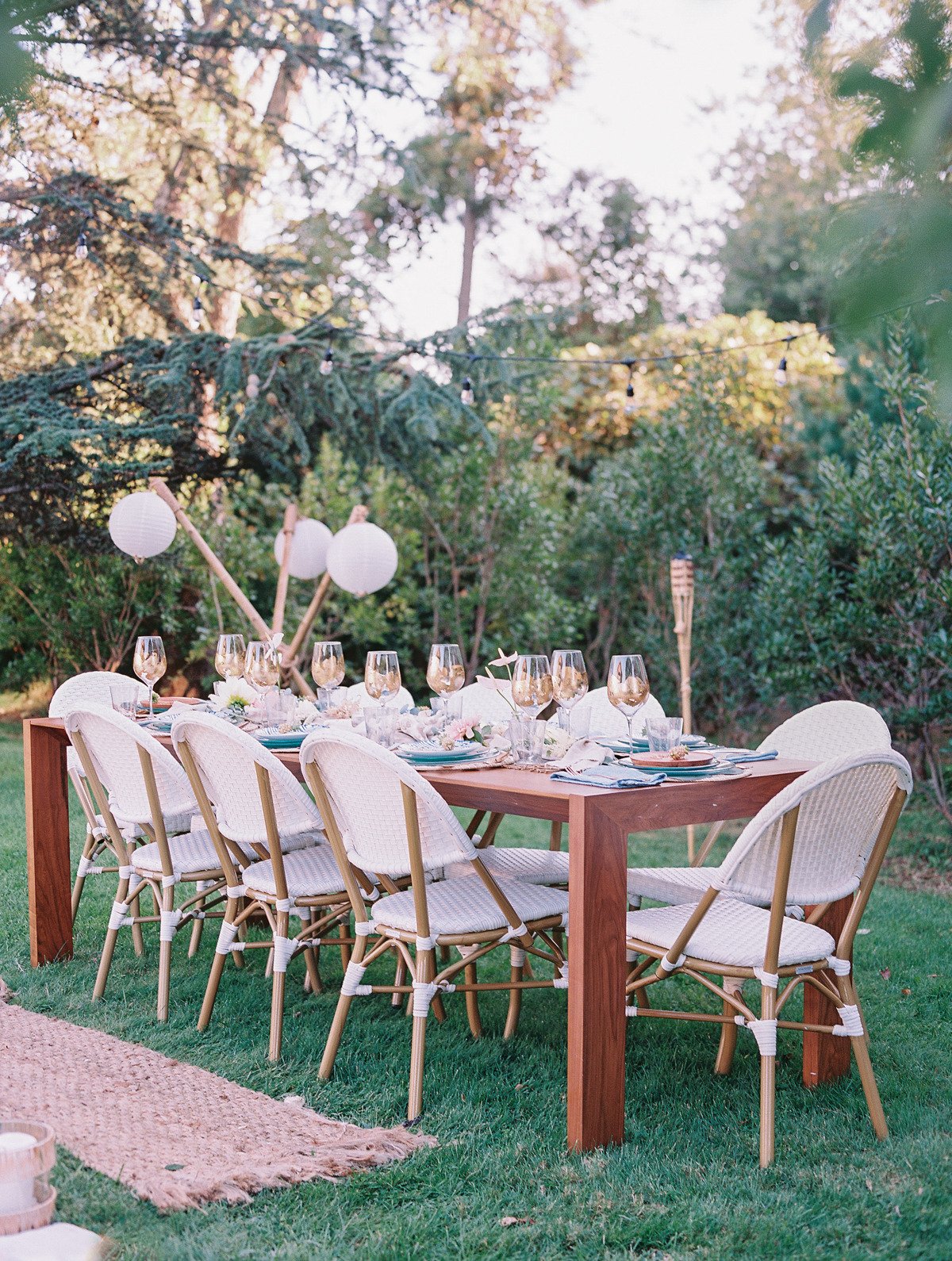 Reception table with rattan chairs, wine glasses, an hanging orbs in the background
