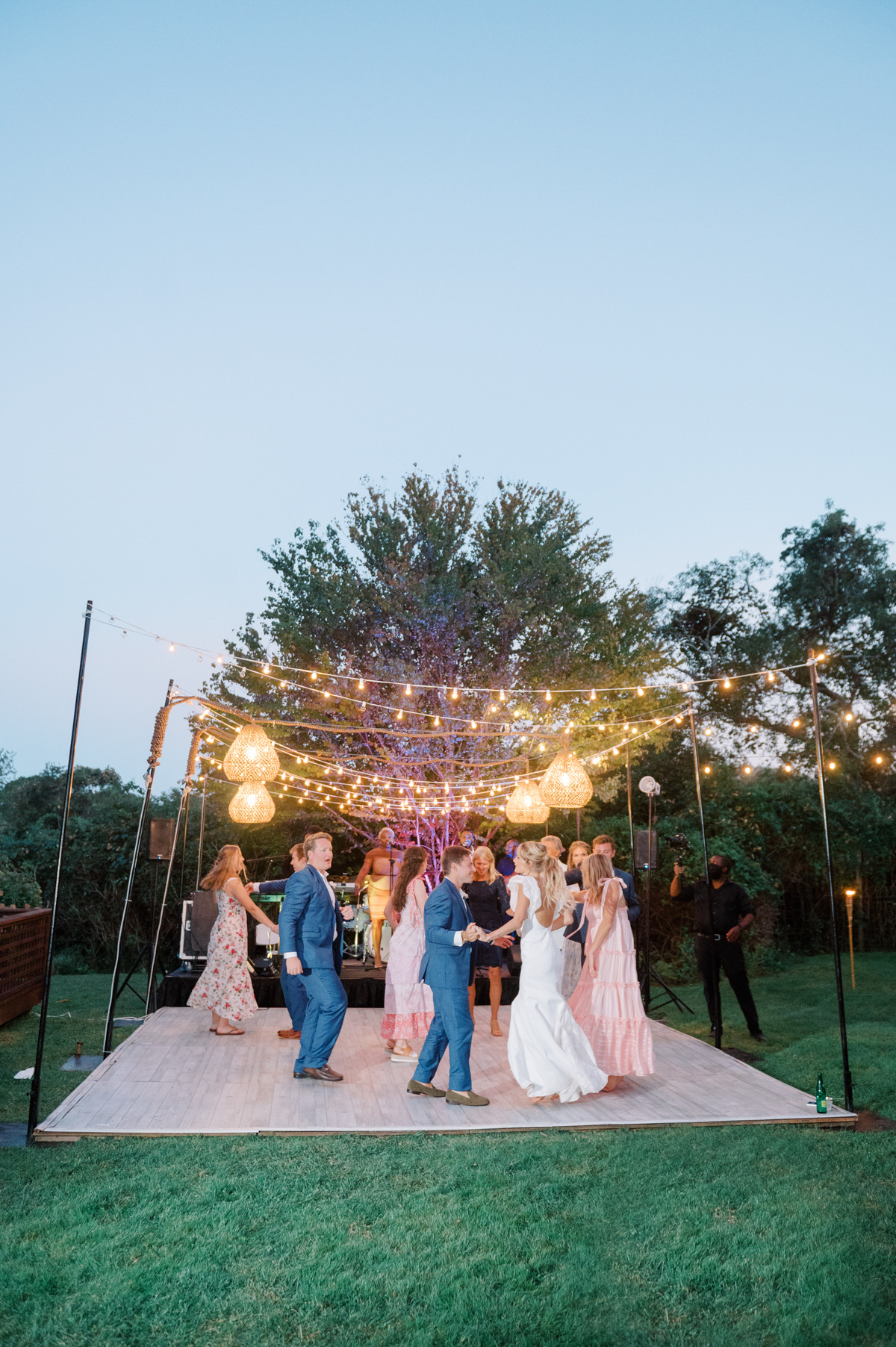 Bride, groom, and guests dancing under string lights and rattan lights
