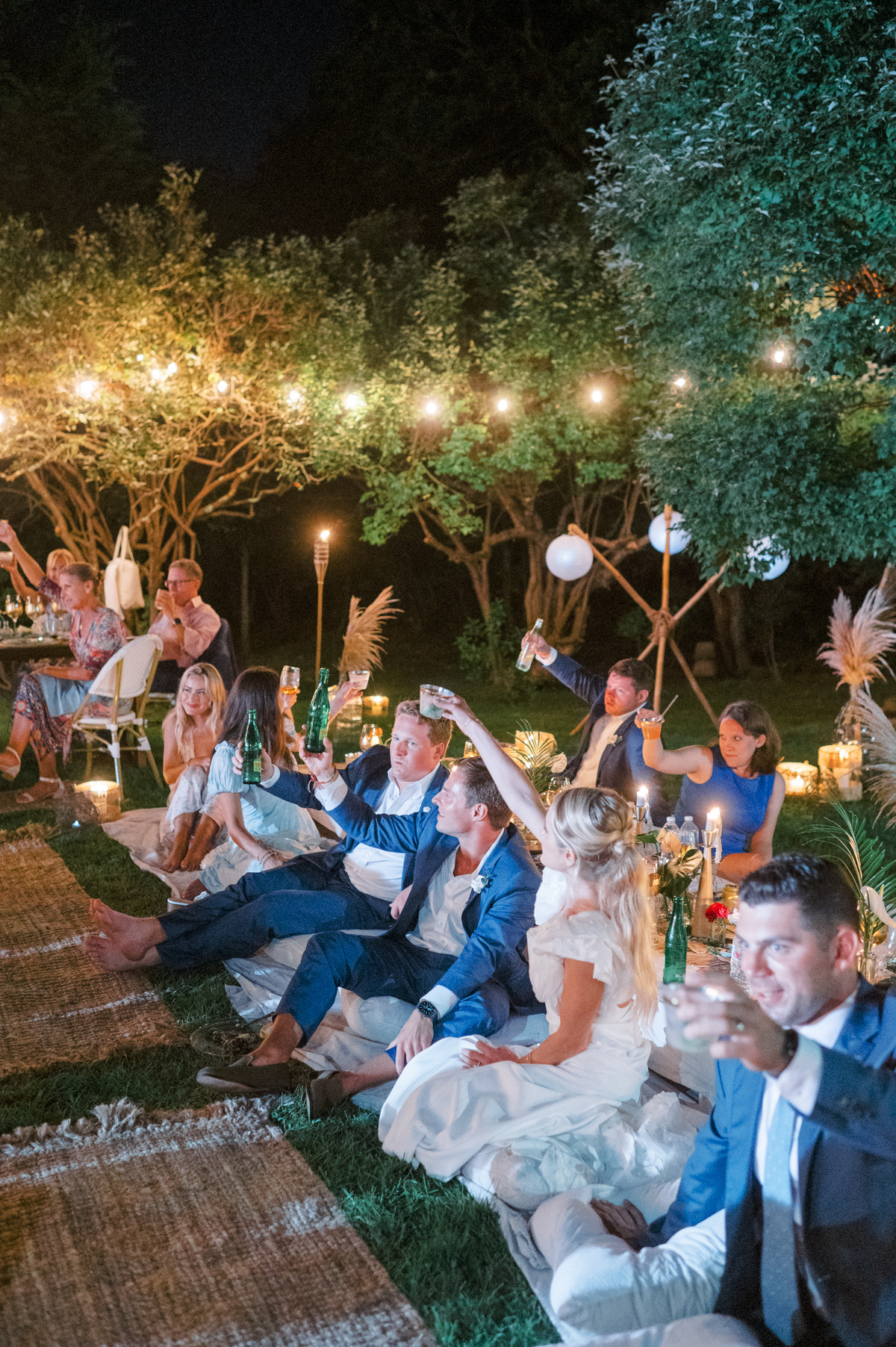Guests and wedding party seated on pillows raising a glass to toast