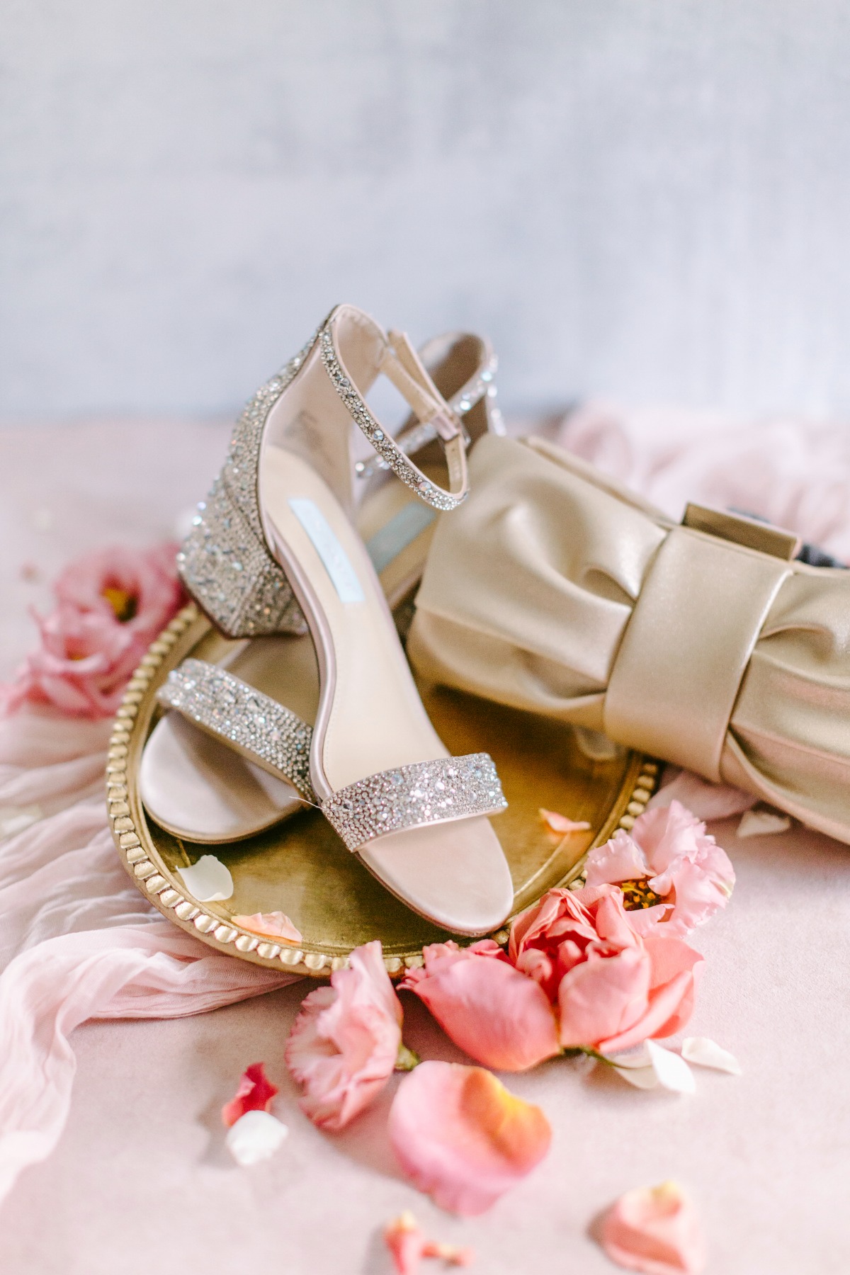 Wedding shoes and purse on gold tray surrounded by pink petals