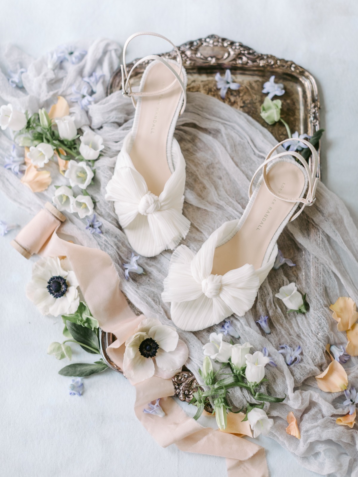 Cream wedding shoes on top of gauze fabric, flowers, and tray