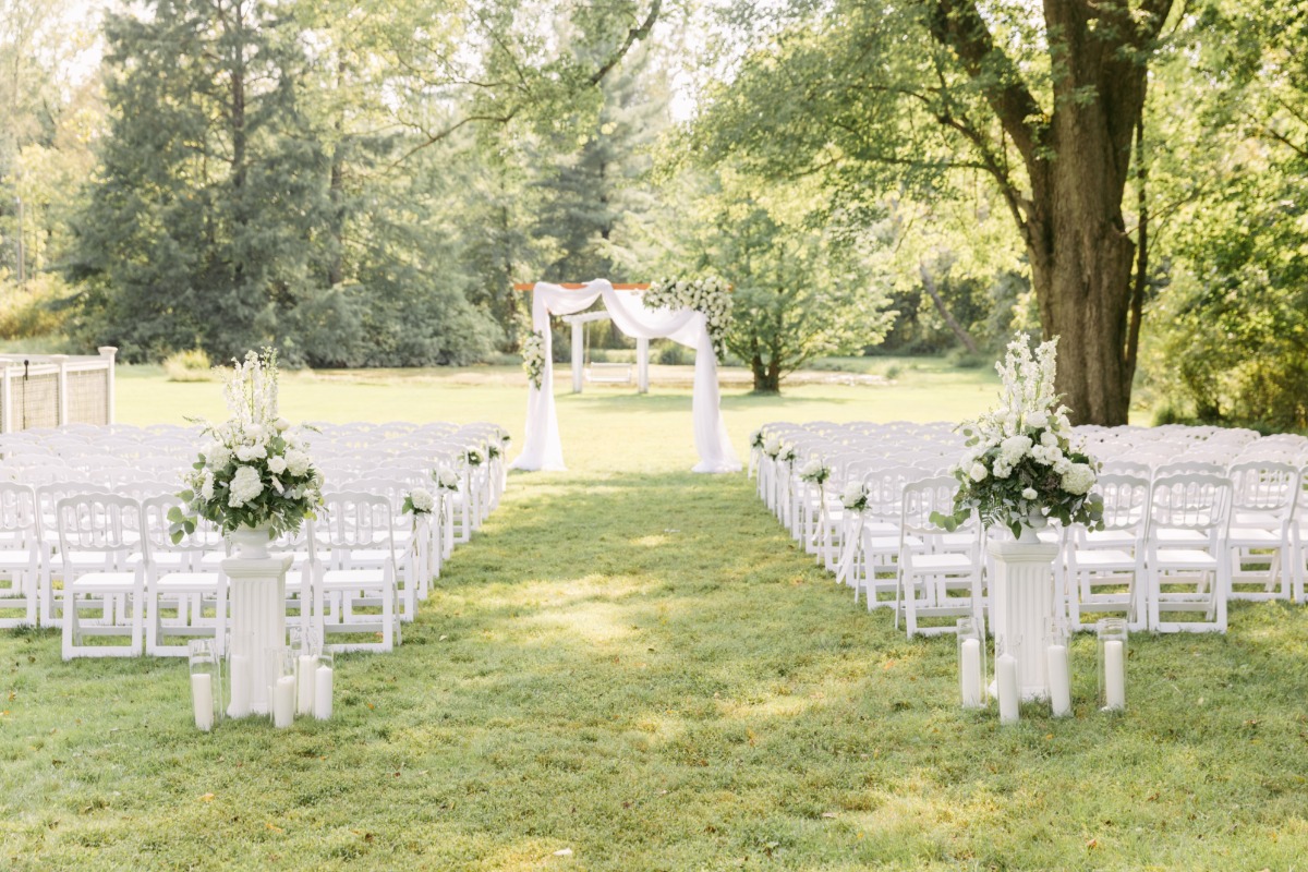 Ceremony space with altar, white floral and candle entryway and white chairs