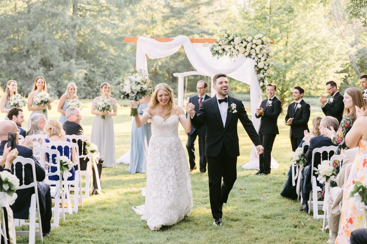 Bride and groom holding hands walking down aisle while guests clap