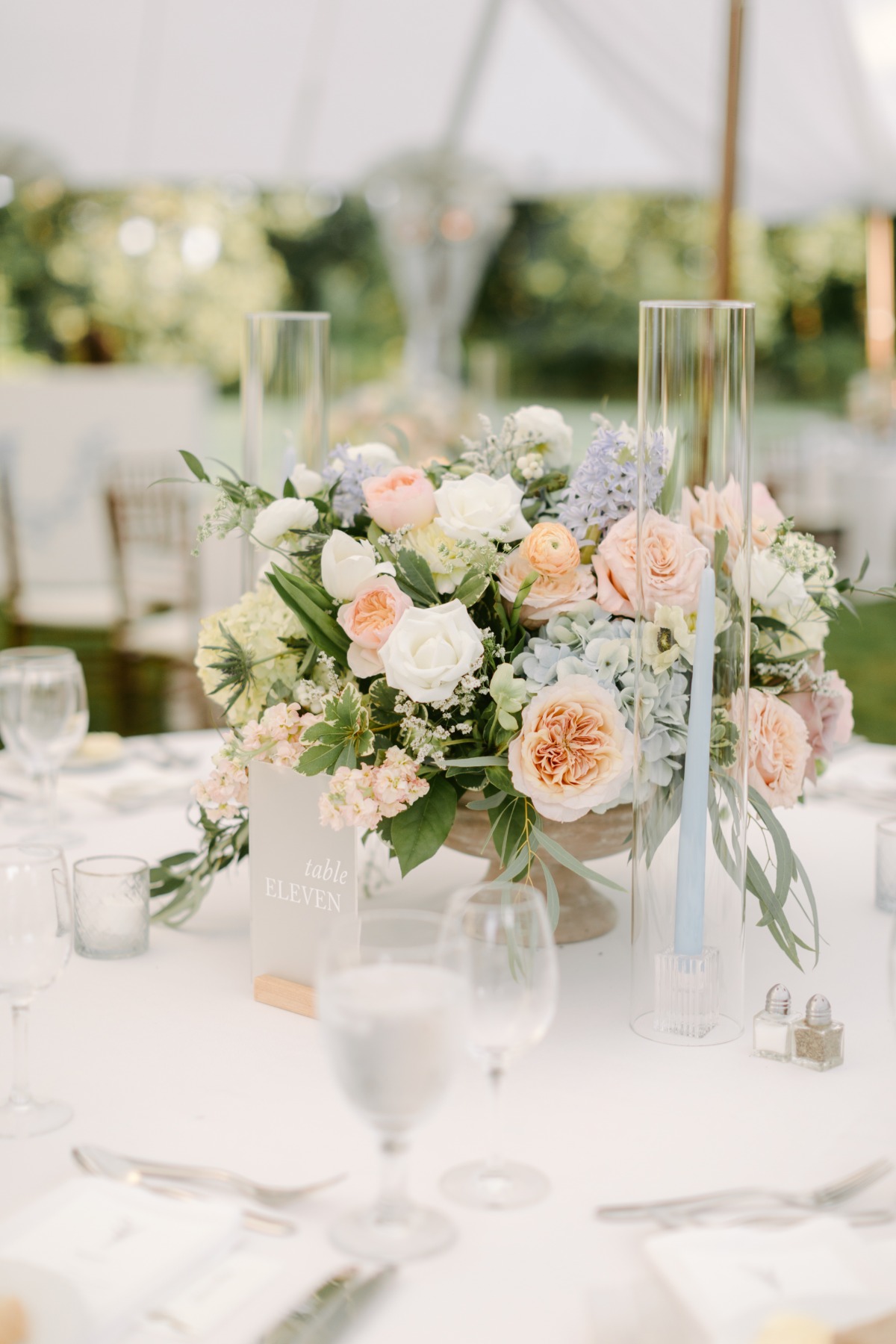 Reception table centerpiece with white, pink, and blue floral arrangements, table number, and candles