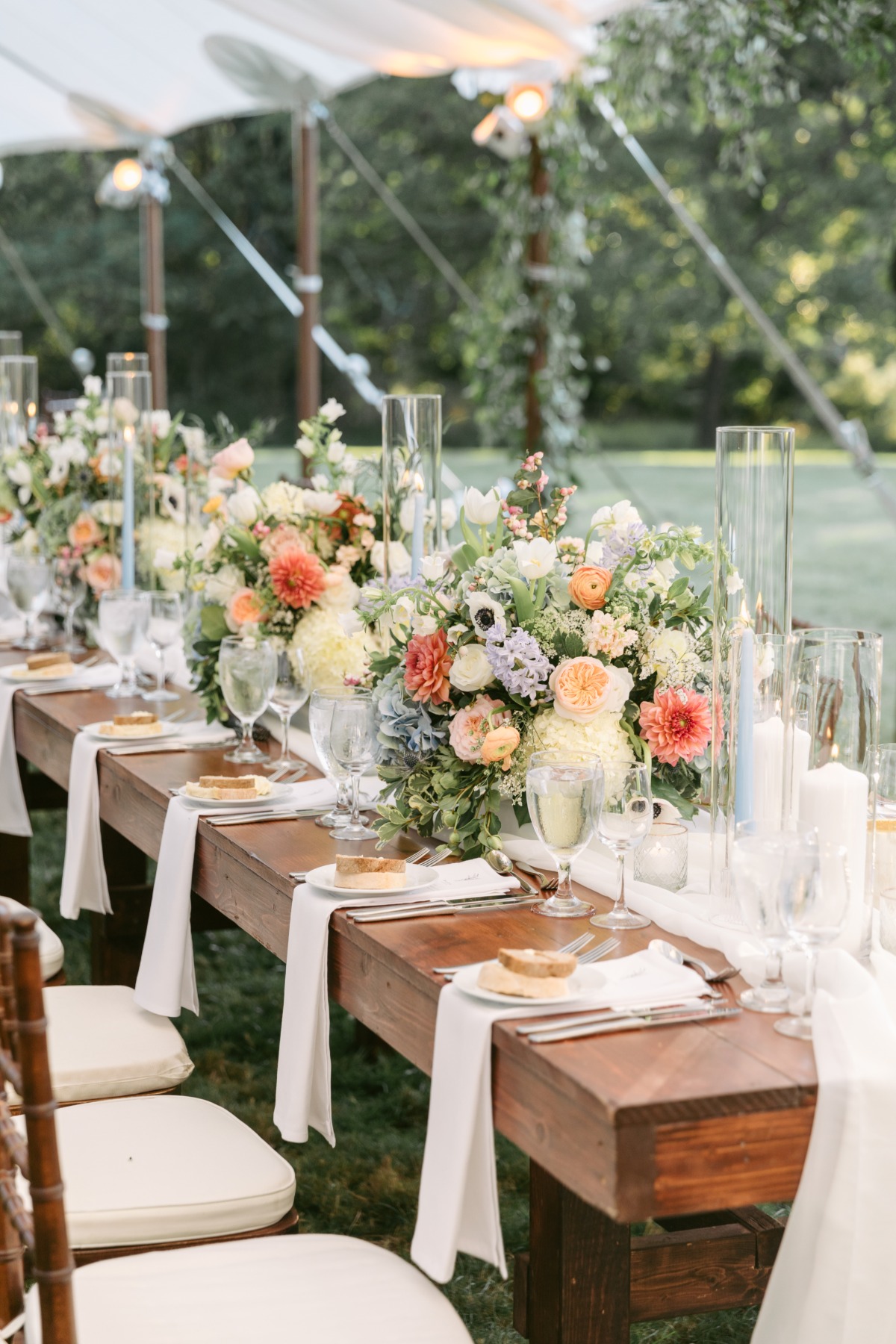 Reception table with floral centerpieces with pops of pink-orange and candles in glass votives
