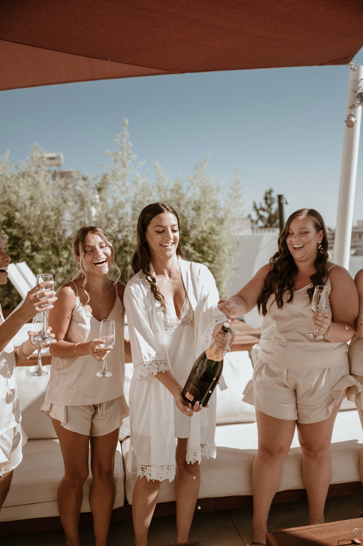 Bride popping champagne bottle with bridesmaids in matching camis and shorts