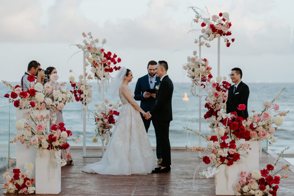 Bride and groom during ceremony surrounded by red and pink flowers