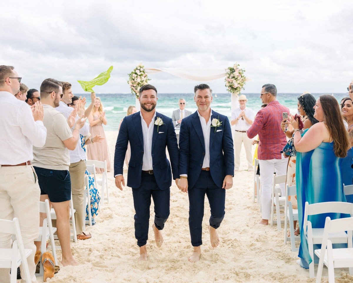 Grooms holding hands walking down aisle after ceremony