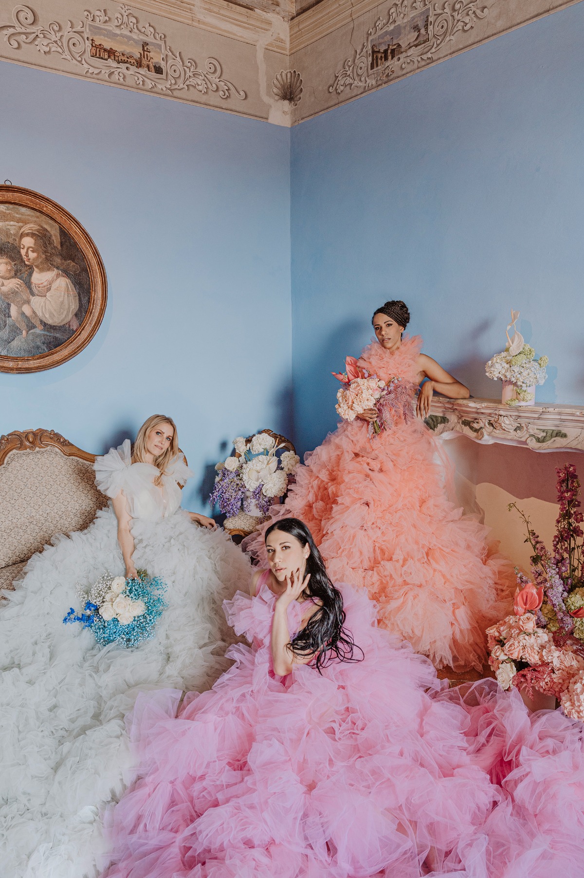 Portrait of three brides in pink, blue-gray, and orange ruffled wedding dresses holding bouquets