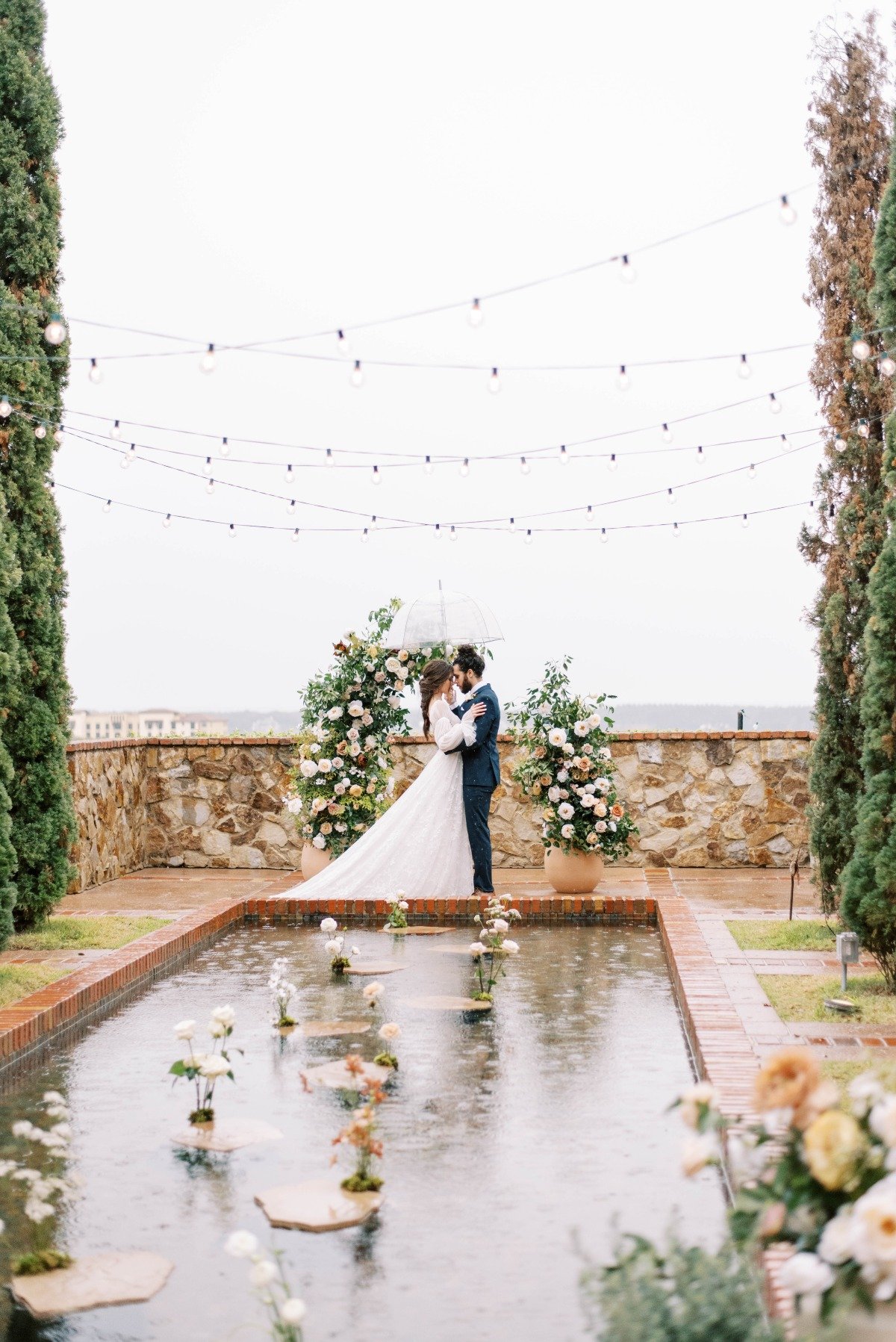 Bride and groom in front of ceremony altar holding clear umbrella
