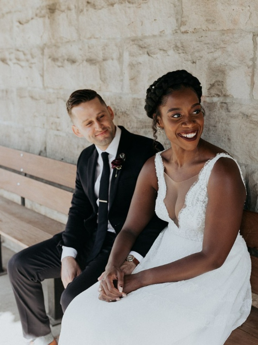 Portrait of bride and groom in front of concrete wall sitting on bench