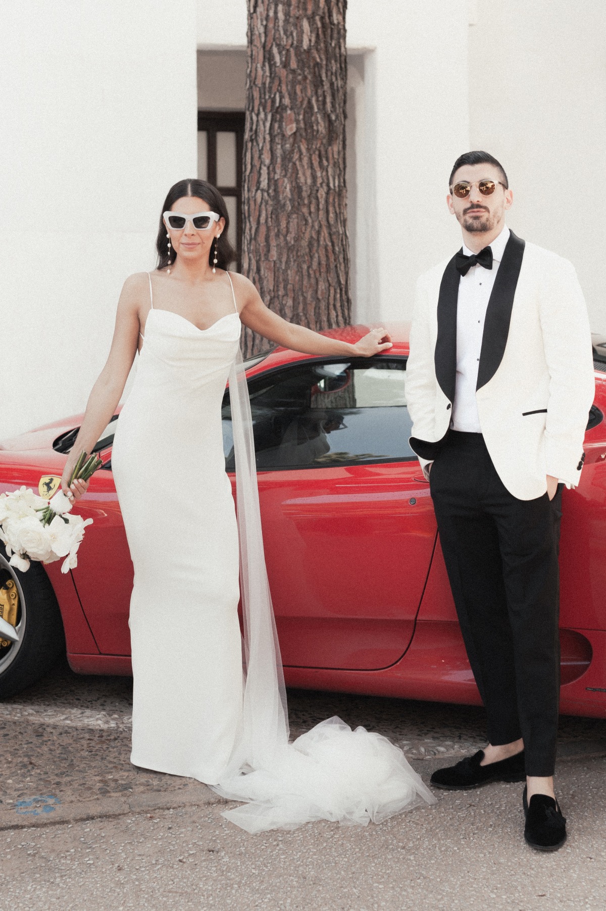 Bride and groom wearing sunglasses in front of red car