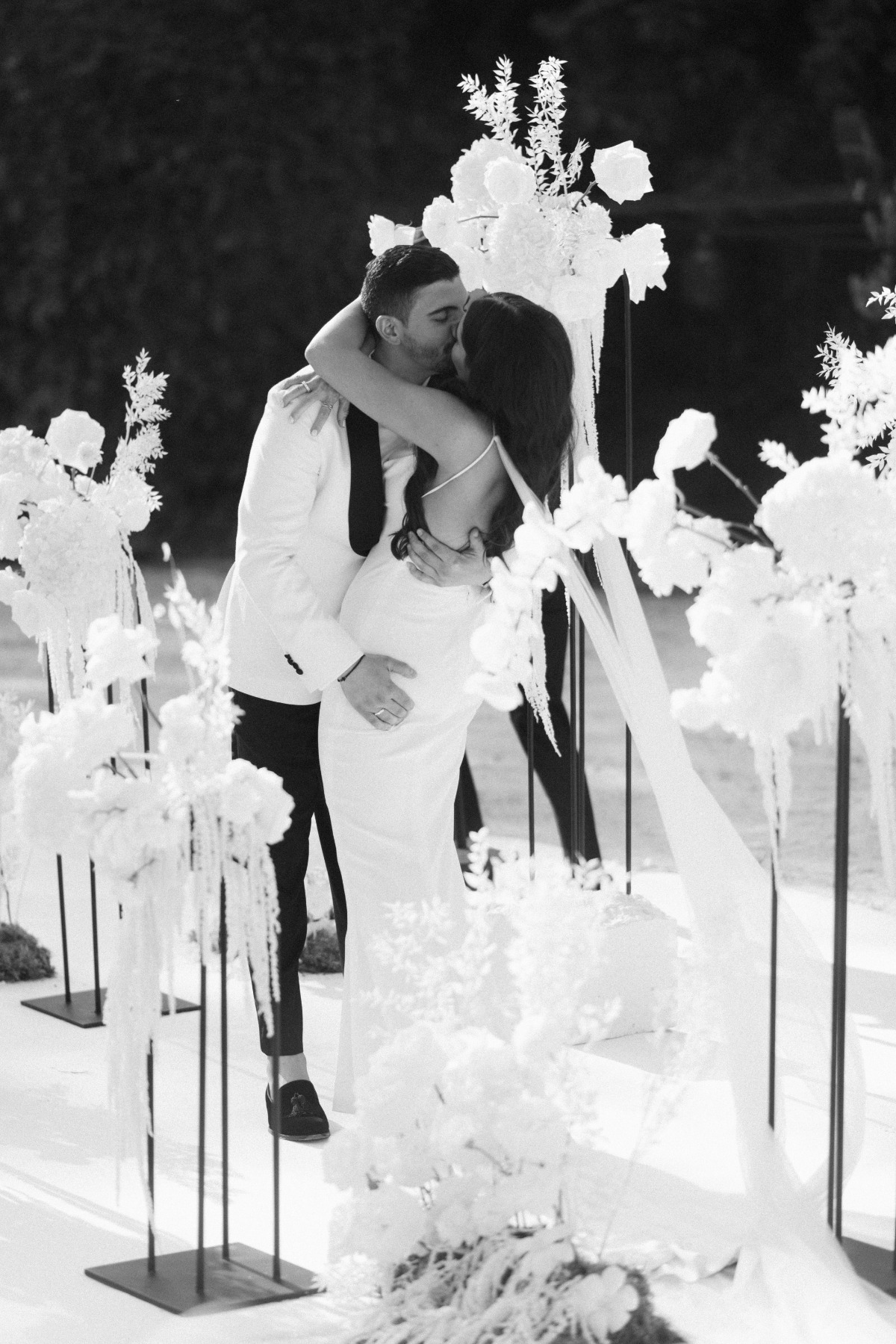 Groom kissing bride during ceremony surrounded by tall vases with white flowers