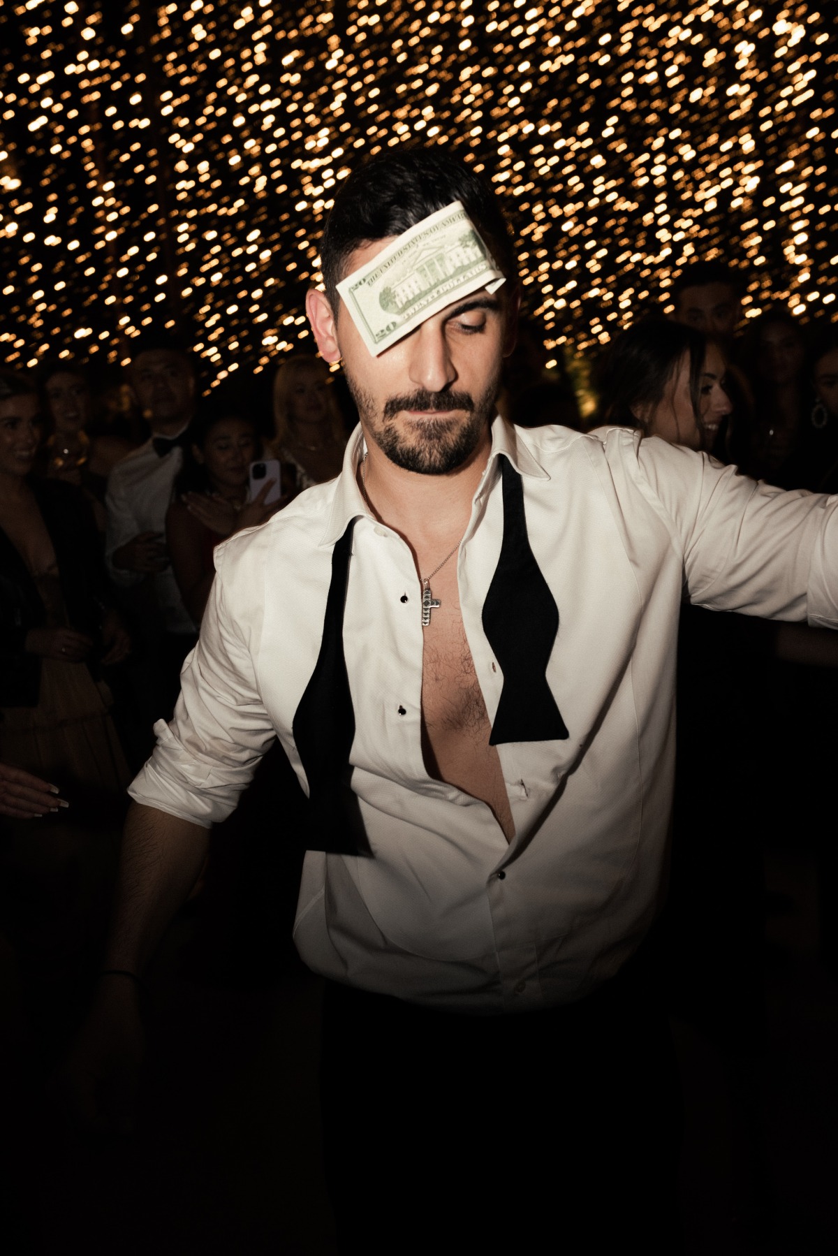 Groom with 20 dollars during Greek tradition on dance floor with shirt unbuttoned