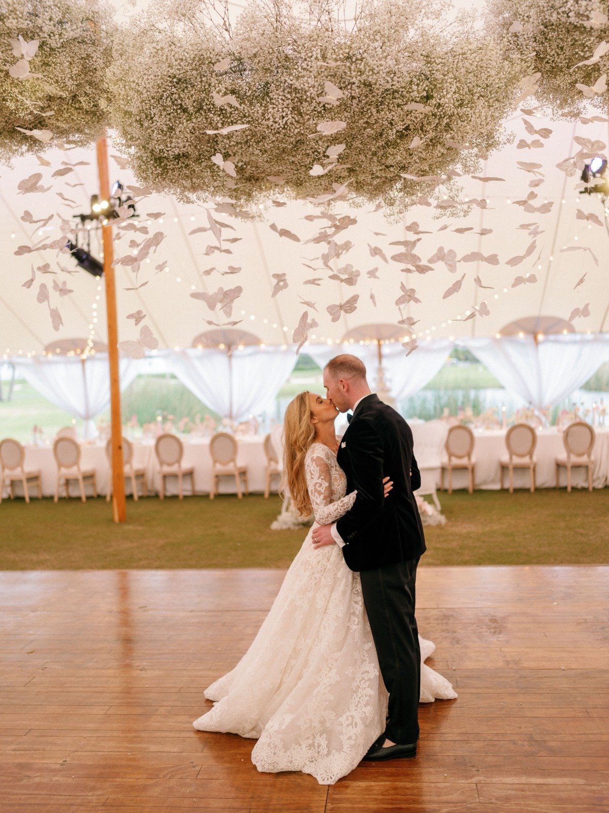Bride and groom kissing on dance floor under baby's breath cloud with hanging butterflies