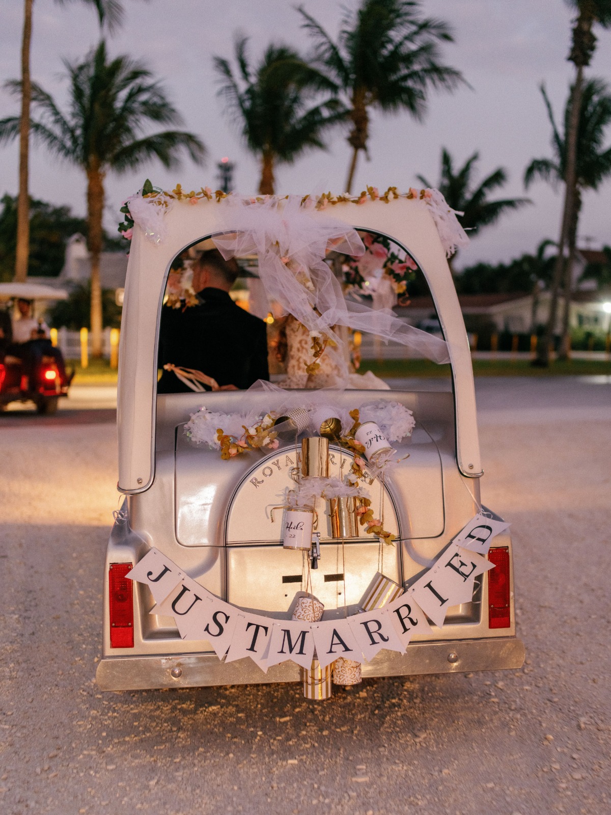 Bride and groom driving away in Rolls-Royce imitation golf cart with Just Married sign