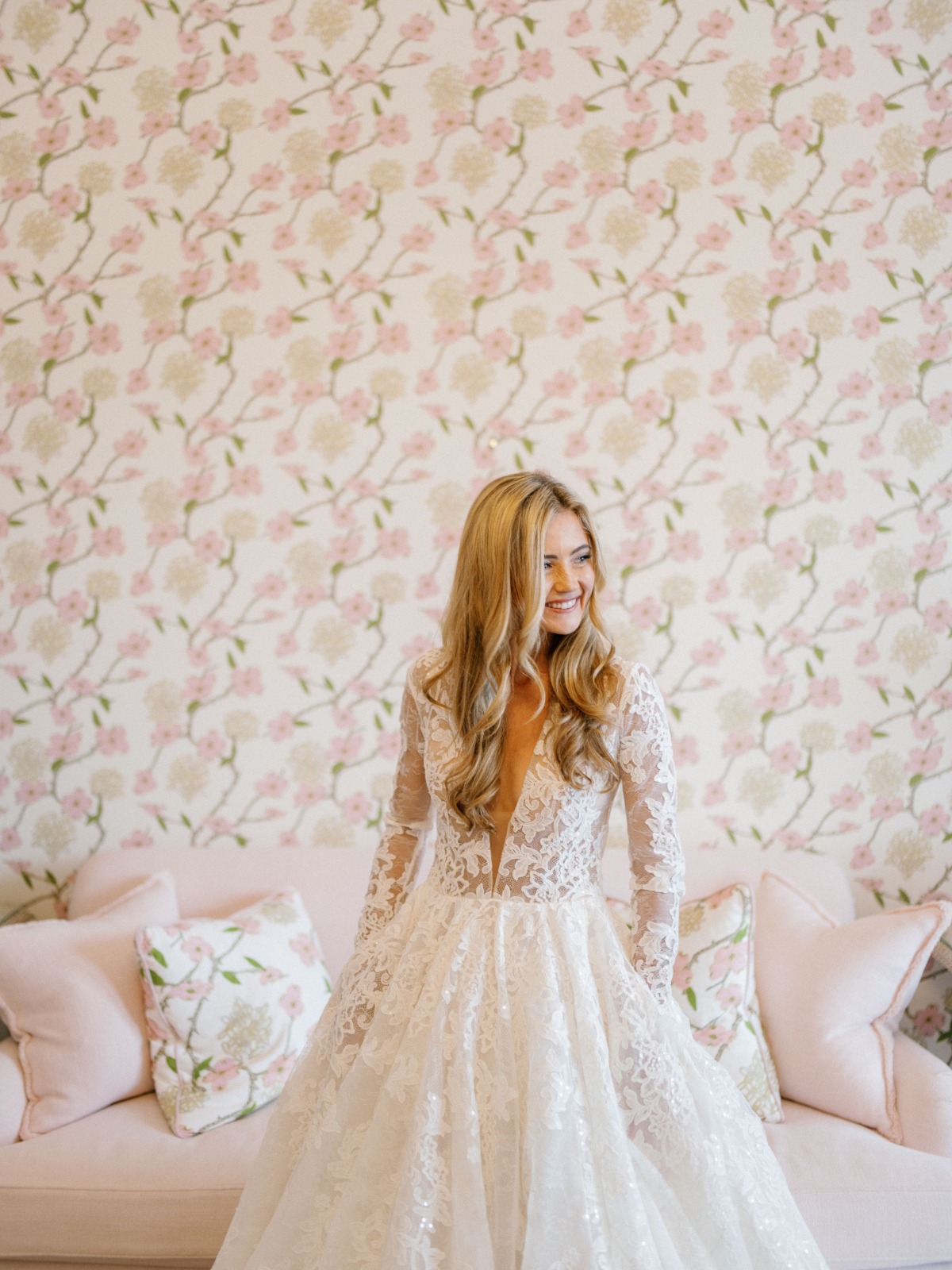 Portrait of bride in wedding dress in front of sofa and printed wallpaper