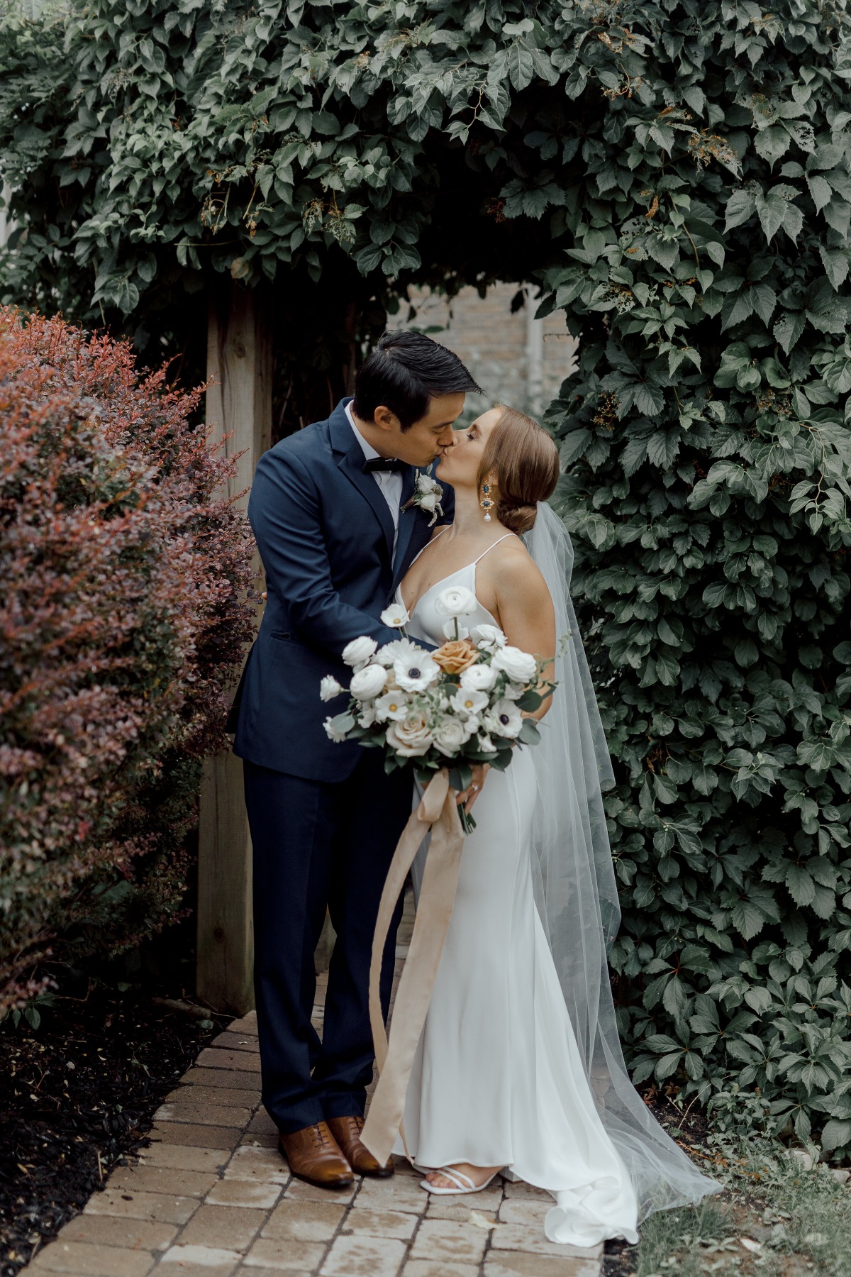Bride and groom kissing in front of ivy walkway