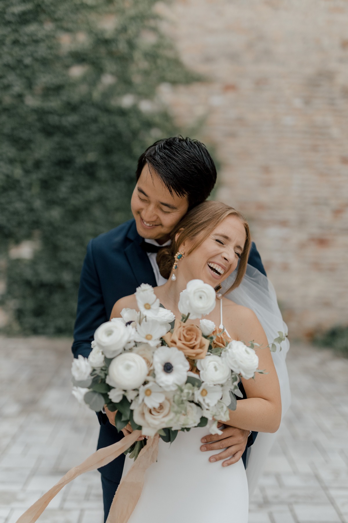 Groom hugging bride from behind holding bouquet