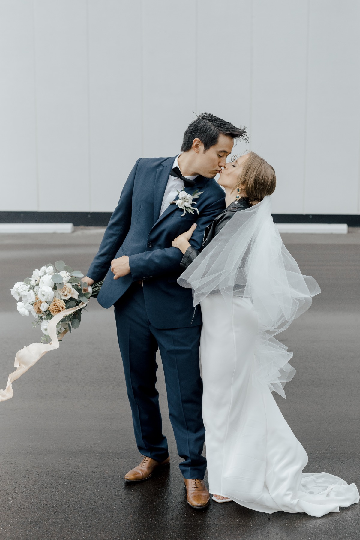 Bride and groom kissing while bride wears leather jacket