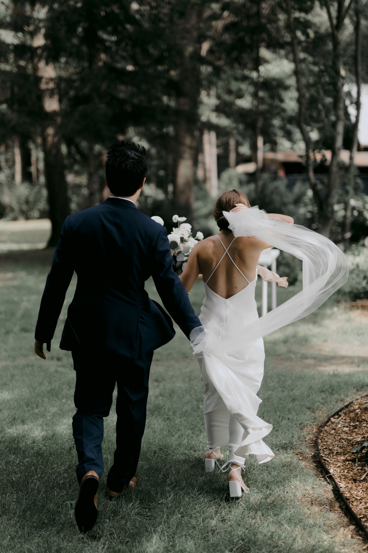 Bride and groom running away from camera with groom holding veil