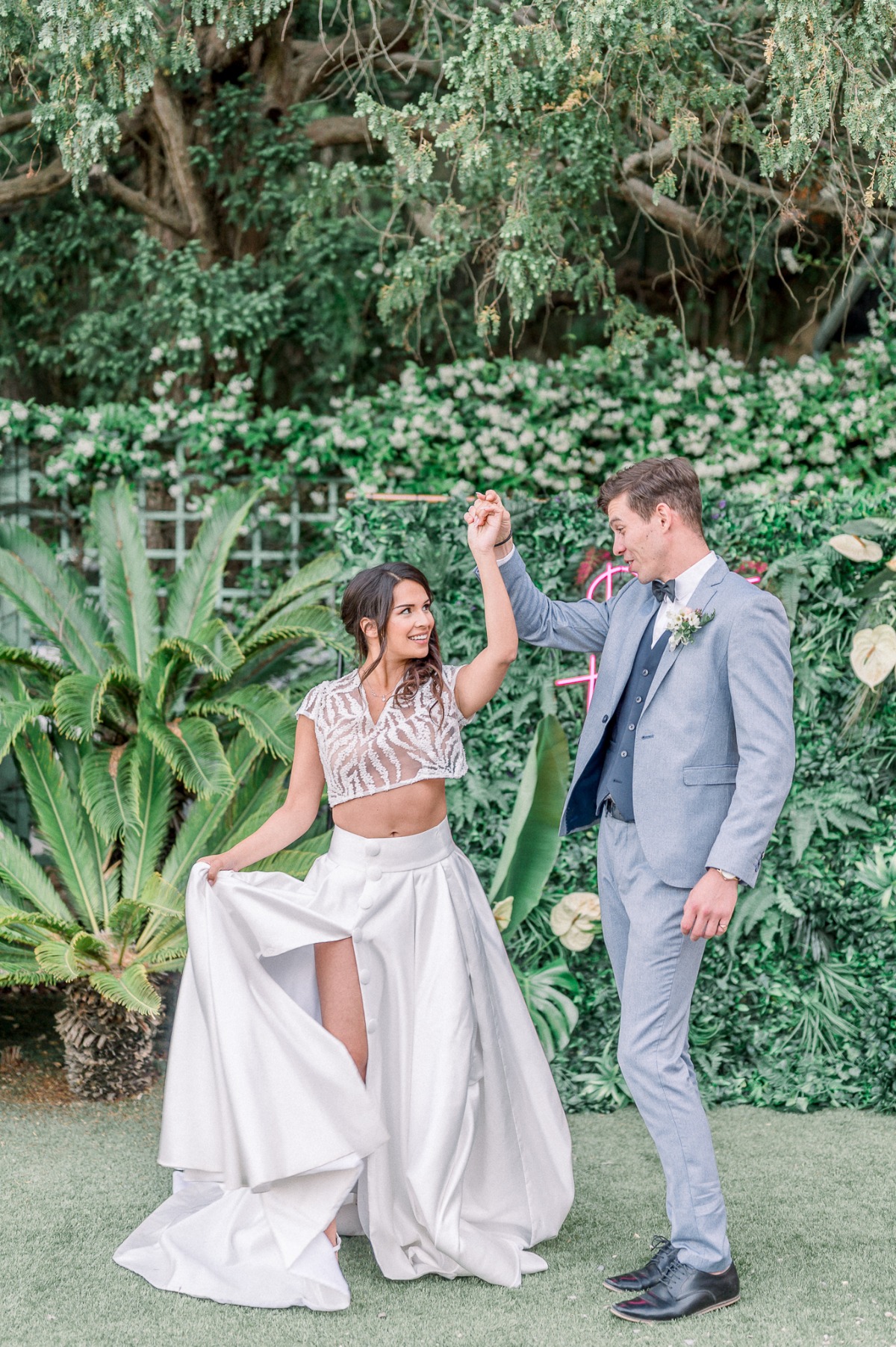 Groom spinning bride in front of tropical plants and neon sign