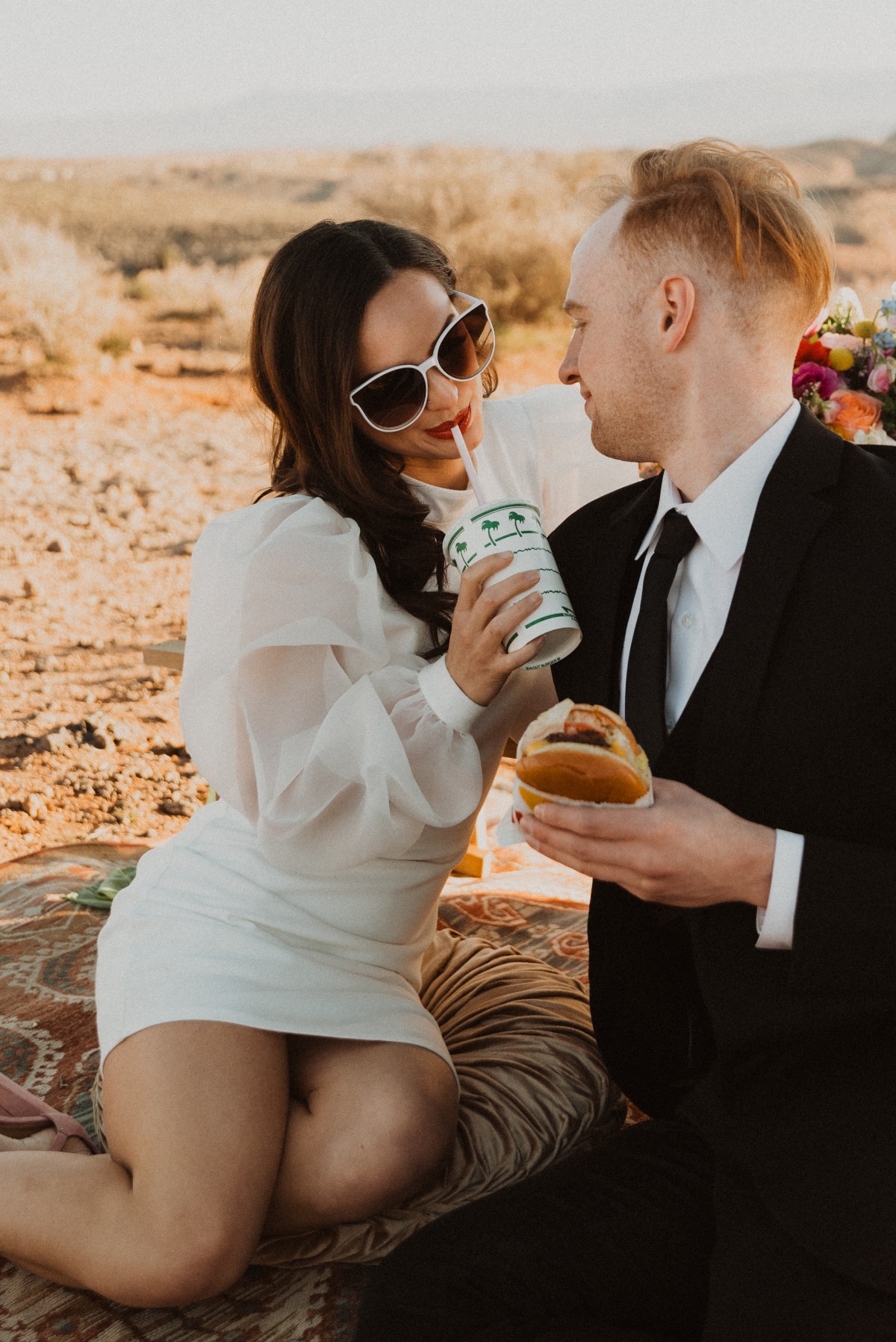 Bride in sunglasses drinking a soda while groom eats an In-n-Out burger