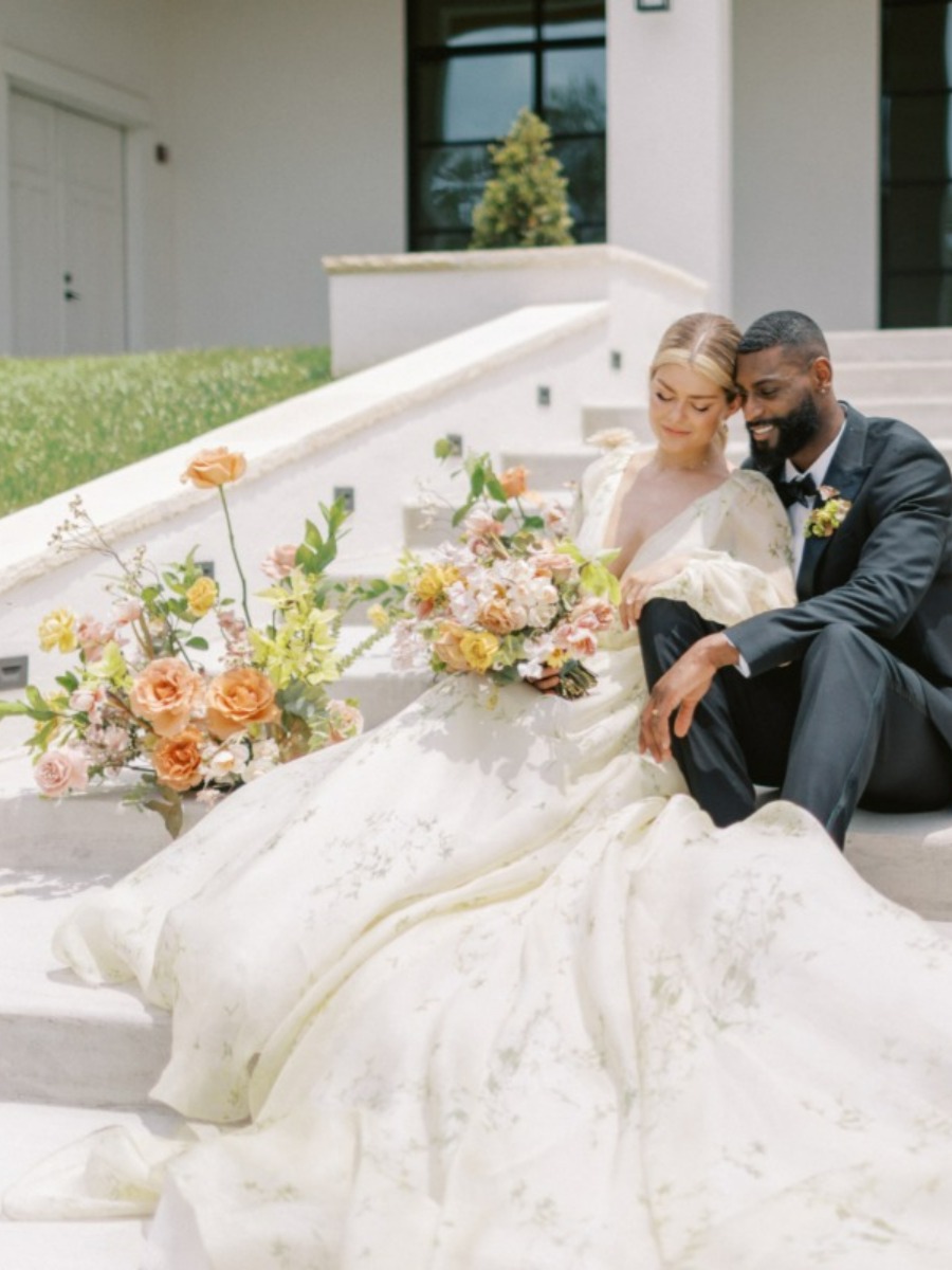 Bride and groom posed on steps surrounded by summer florals and bouquet