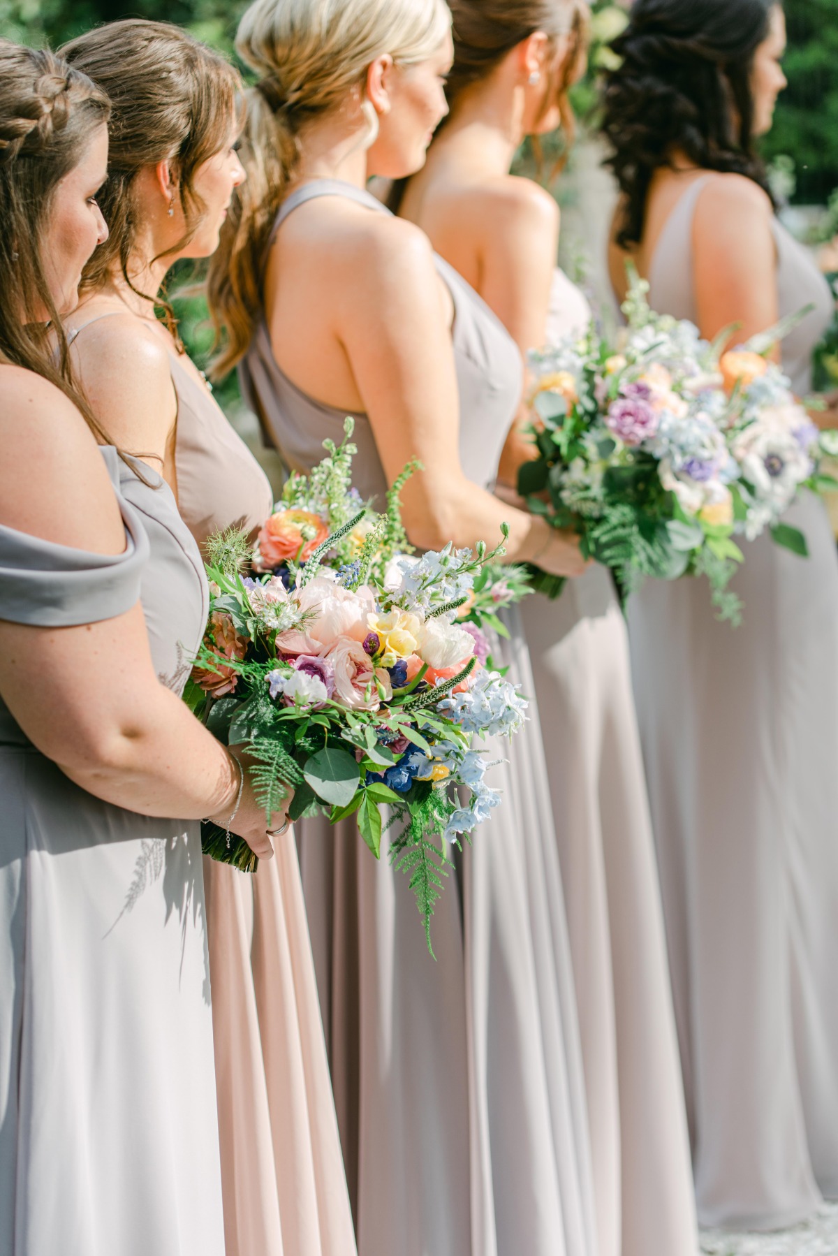 Row of bridesmaids in neutral dresses holding bouquets at altar