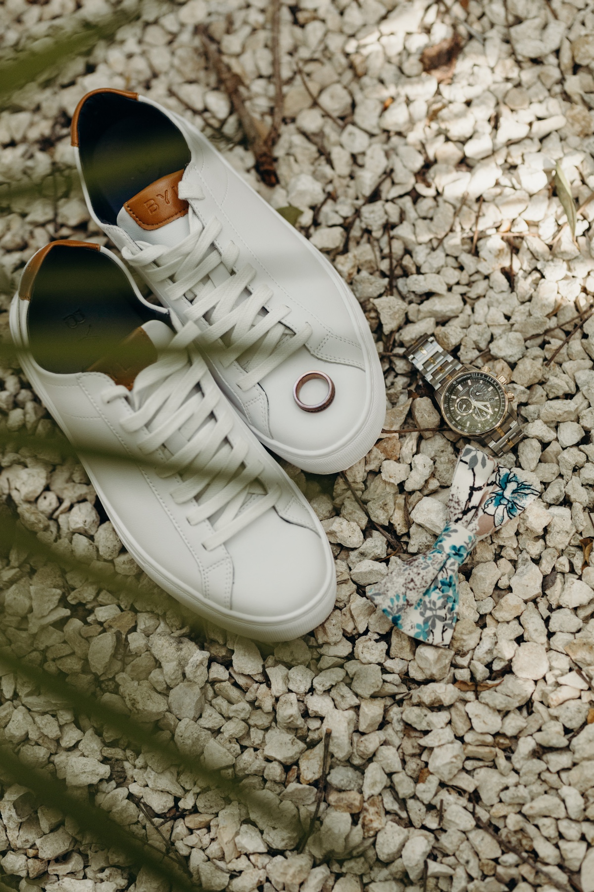 Groom's sneakers, watch, wedding band, and bow tie on rocks