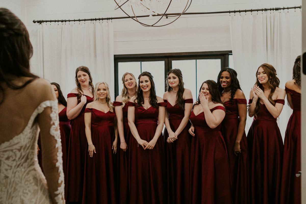 Bridesmaids in burgundy dresses seeing bride for first time