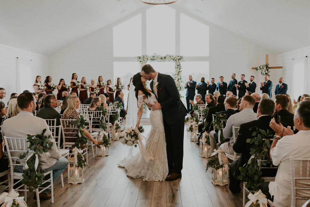 Groom kissing bride after ceremony midway down aisle