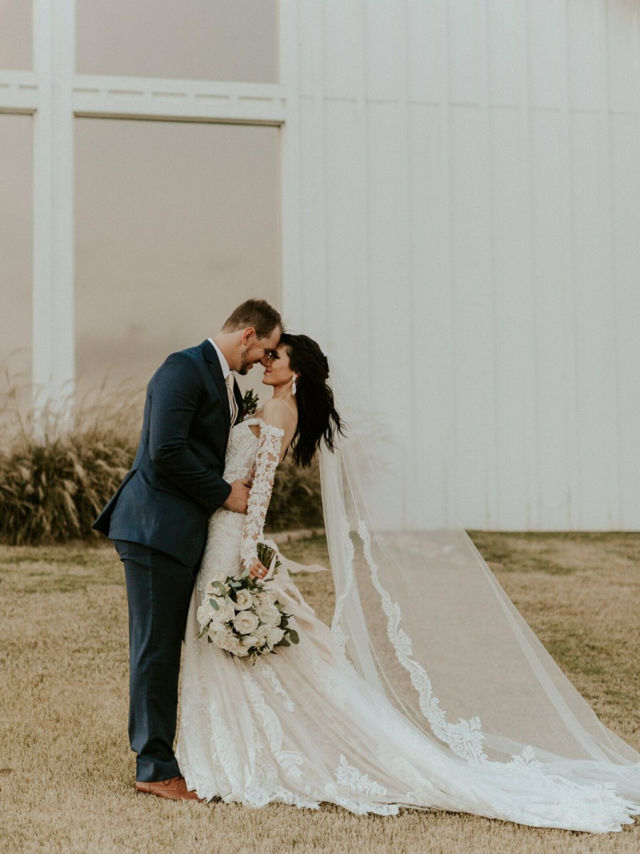 Bride and groom nose to nose in front of white barn