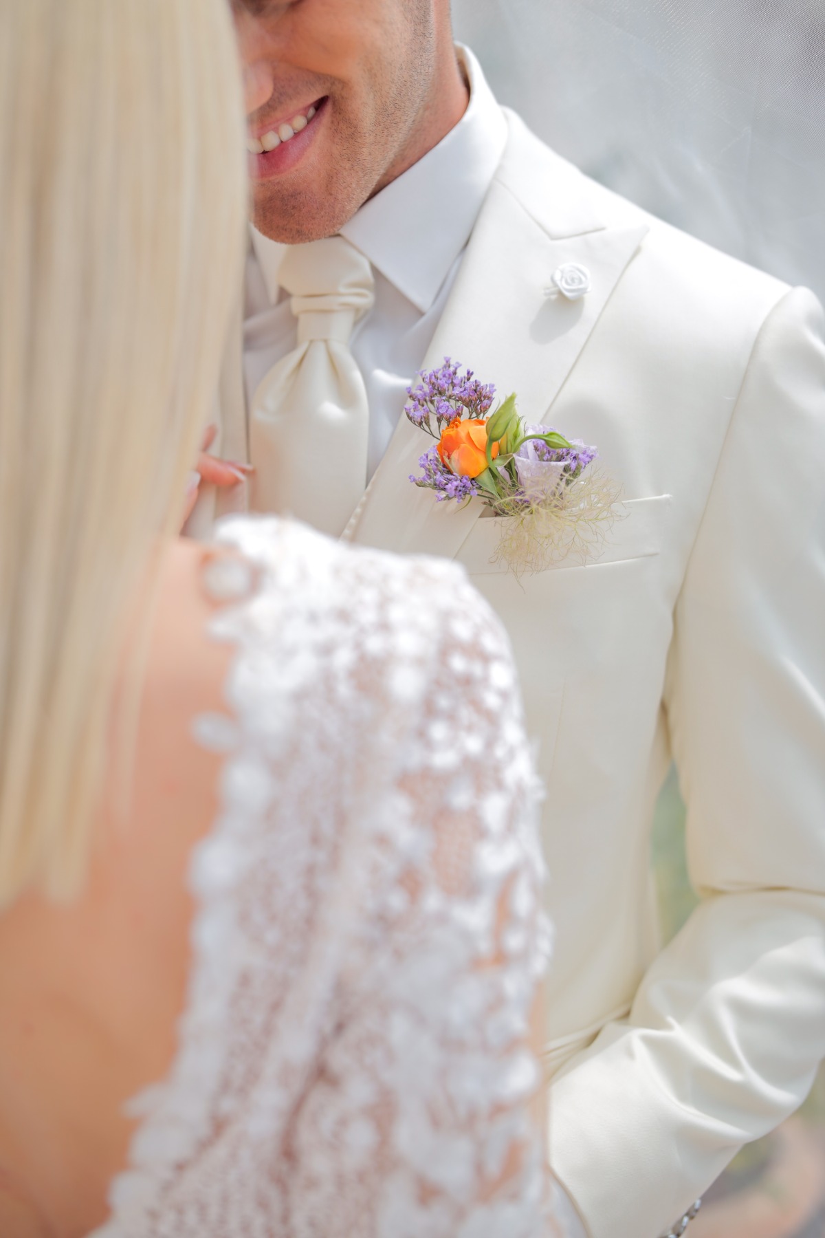 Close-up of grooms white suit with colorful boutonniere 