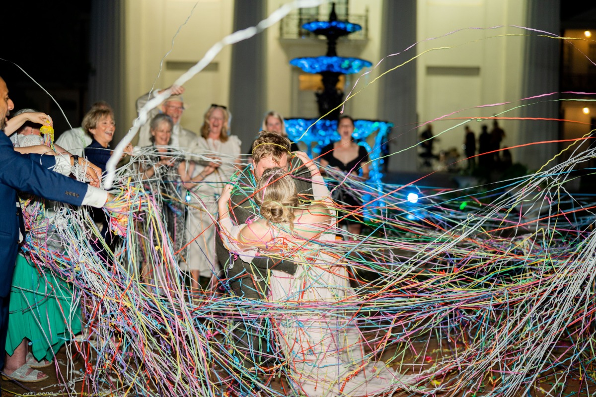 Bride and groom kissing under rainbow silly string