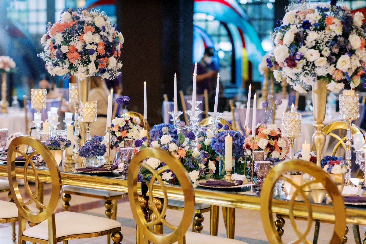Reception table setting with floral centerpieces, gold chairs, and candles