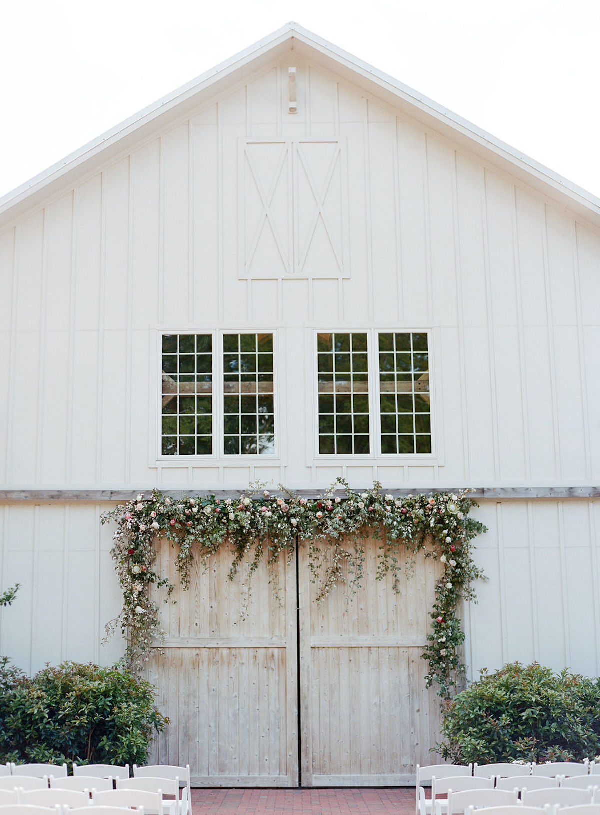 Barn doors with greenery and floral arch with chairs in front for ceremony