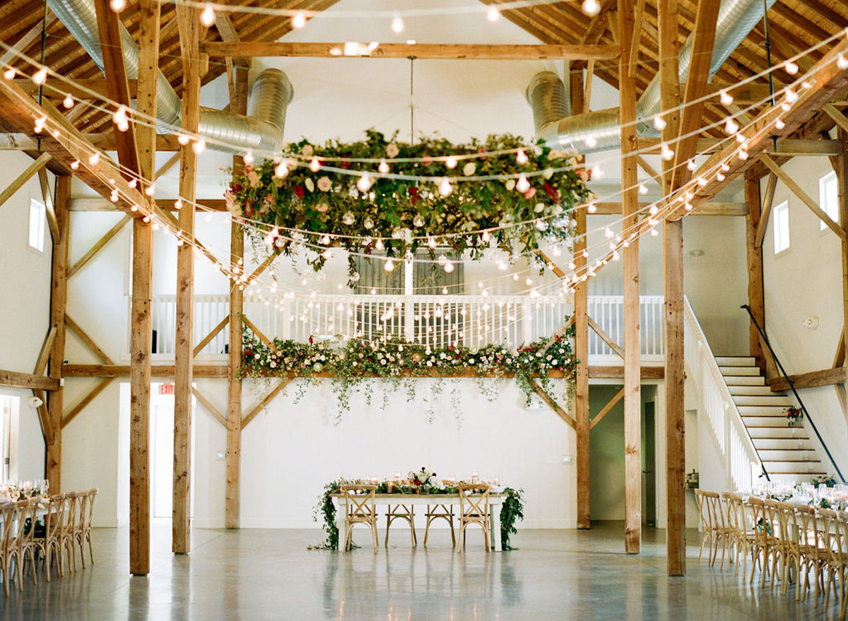 Panoramic view of reception space with hanging greenery, string lights, and long tables