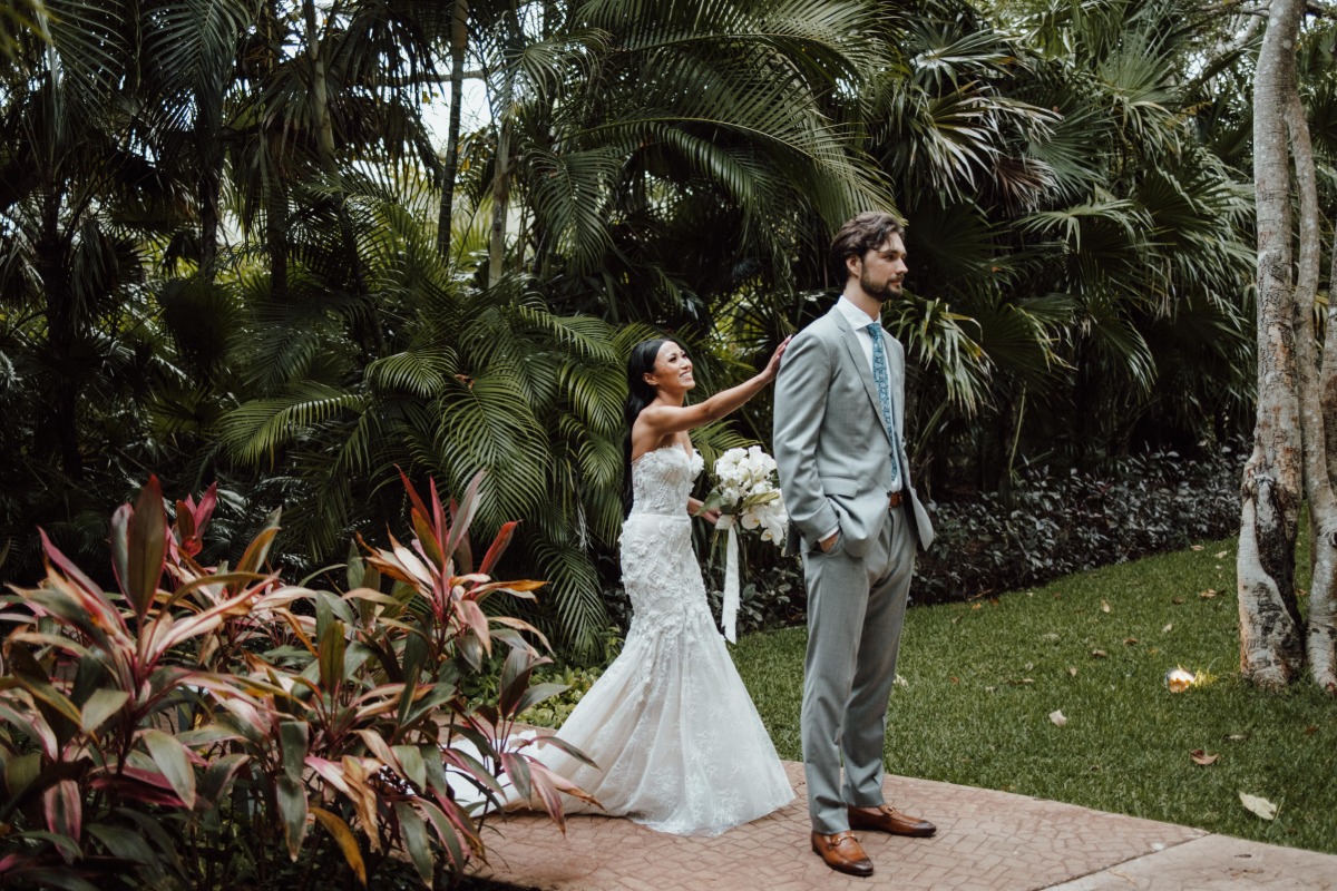 Bride holding bouquet tapping groom on shoulder for first look