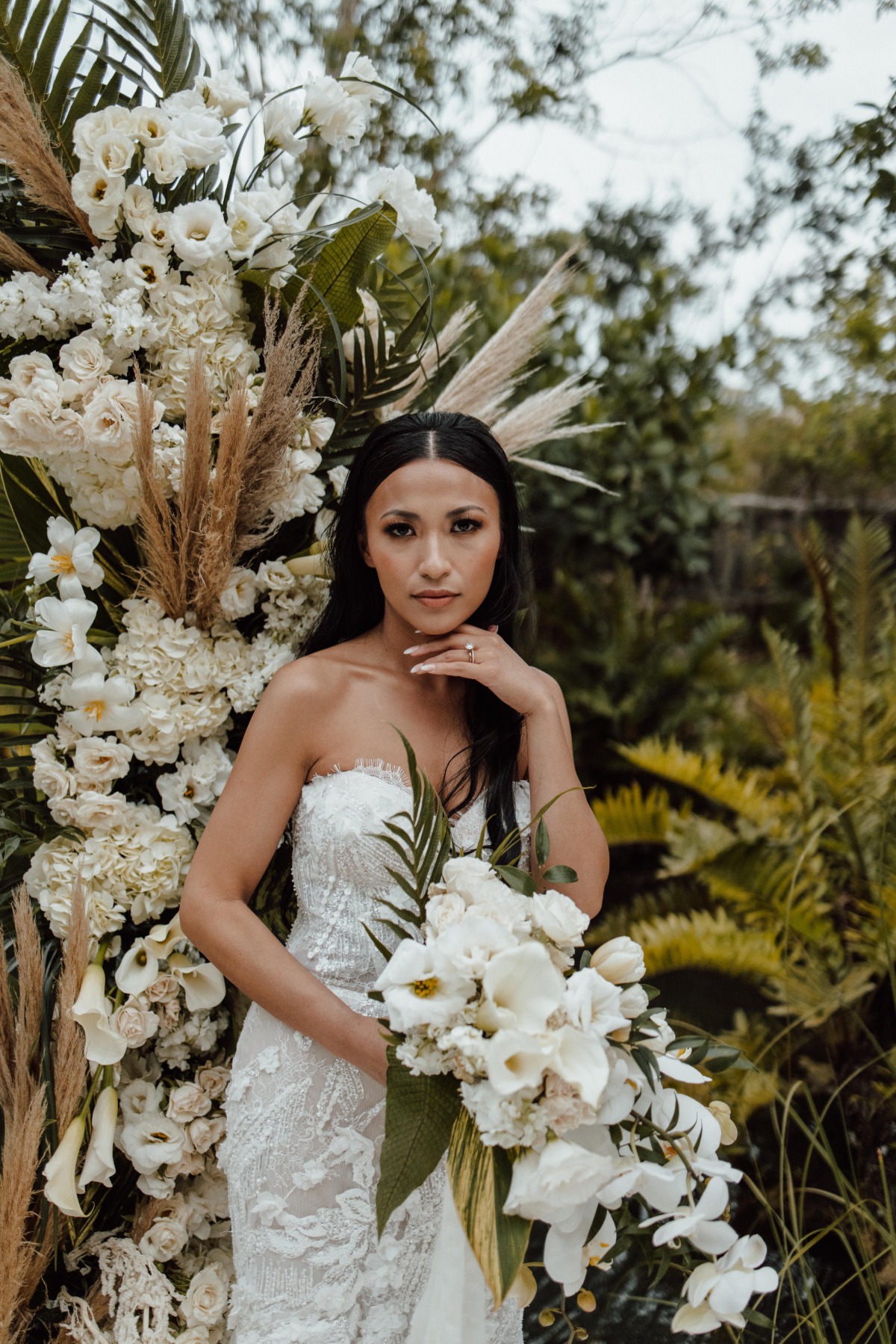 Bridal portrait in front of white flower and tropical foliage installation