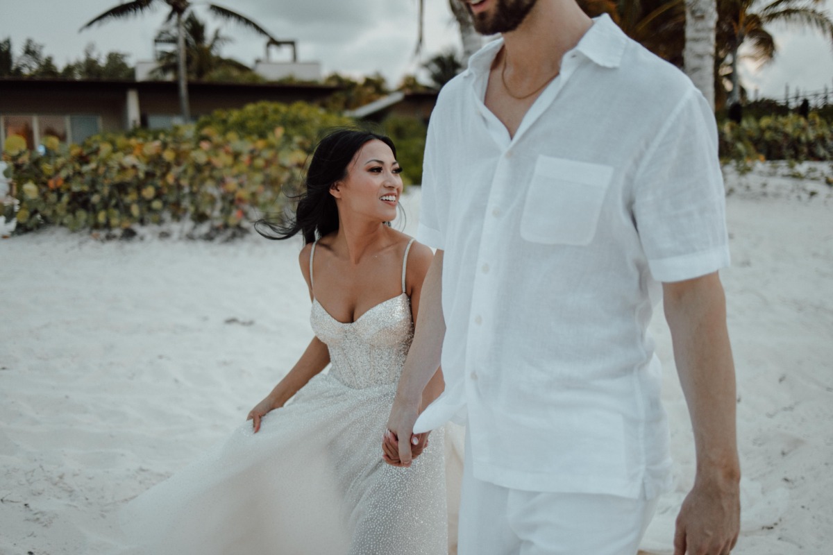 Bride and groom holding hands walking on beach